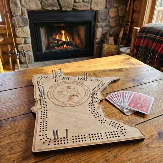 Minnesota-shaped cribbage board, hunting and fishing emblem design - set up for play on a rustic cabin table by the fireplace, lifestyle shot
