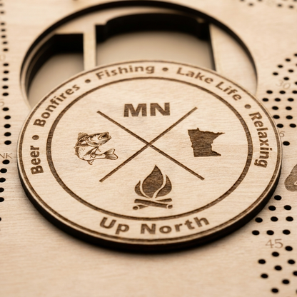Minnesota-shaped cribbage board - close-up of the engraved Up North emblem with fish and campfire icons, studio macro shot