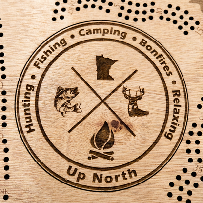 Minnesota-shaped cribbage board, hunting and fishing emblem design - close-up of the engraved fish, deer, and campfire icons, studio macro shot